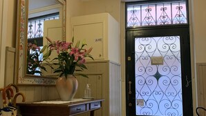 Una habitación con un escritorio de madera, un jarrón con flores, un espejo y una puerta con un panel de vidrio decorativo.