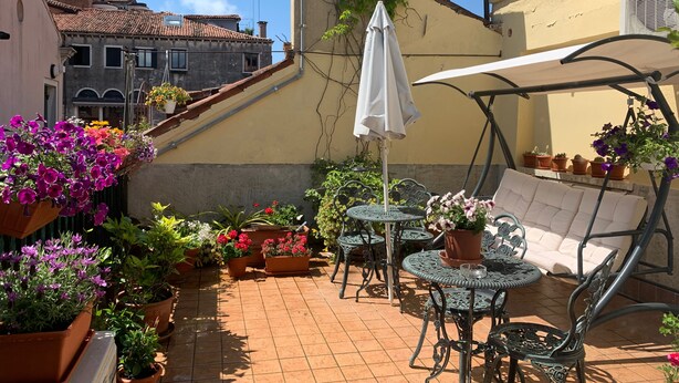 Un patio con mobiliario exterior, plantas en macetas y vistas de los edificios circundantes.