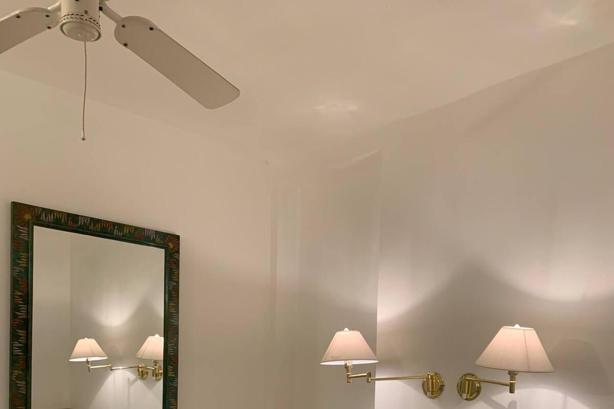 Hotelkamer met een bed, een plafondventilator, een spiegel aan de muur en twee wandlampen.