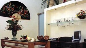 Un comedor con una mesa de madera, sillas, un jarrón con flores y una estantería con vasos.