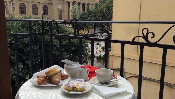 Un balcón con una mesa dispuesta para el desayuno, que incluye croissants, una jarra, una taza y un plato con bollería.