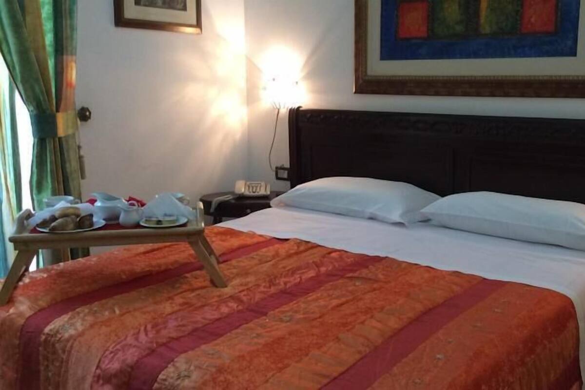 Una habitación de hotel con una cama, una mesita de noche con una bandeja de pasteles, una lámpara y un cuadro en la pared.