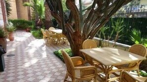 An outdoor patio area with checkered flooring, wicker furniture, and potted plants. - Hotel Villa Archirafi (Palermo)