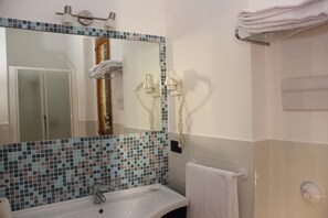A bathroom with a tiled backsplash, a sink, a mirror, a towel rack, and a shower area. - Hotel Villa Archirafi (Palermo)