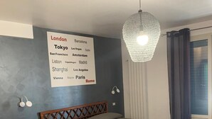 A bedroom with a bed, a chair, a nightstand, a wall-mounted lamp, and a sign listing various cities. - Hotel Villa Archirafi (Palermo)