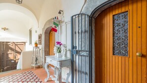A wooden door with a decorative metal gate, a white table with a vase of flowers, and a tiled floor. - Orchid Corner (Meta)