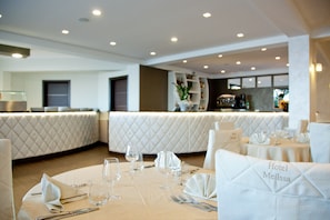 A restaurant with white upholstered booths, tables set with wine glasses, cutlery, and napkins. - Melissa (Melissa)