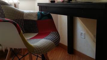 A chair with a woven seat and wooden legs, a black desk with a television displaying a car, and a wooden floor.