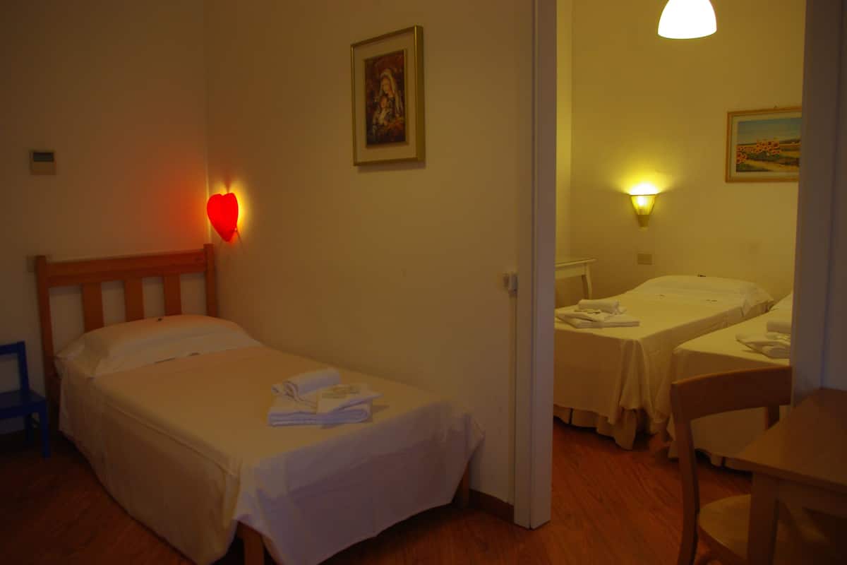 A hotel room with two single beds, a wooden chair, a small table, and a wall-mounted light.
