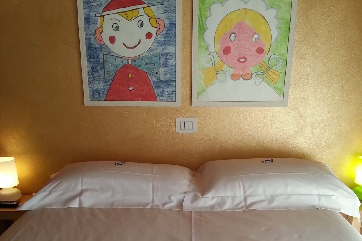 A hotel room with a large bed, white linens, a folded towel, and two wall paintings.