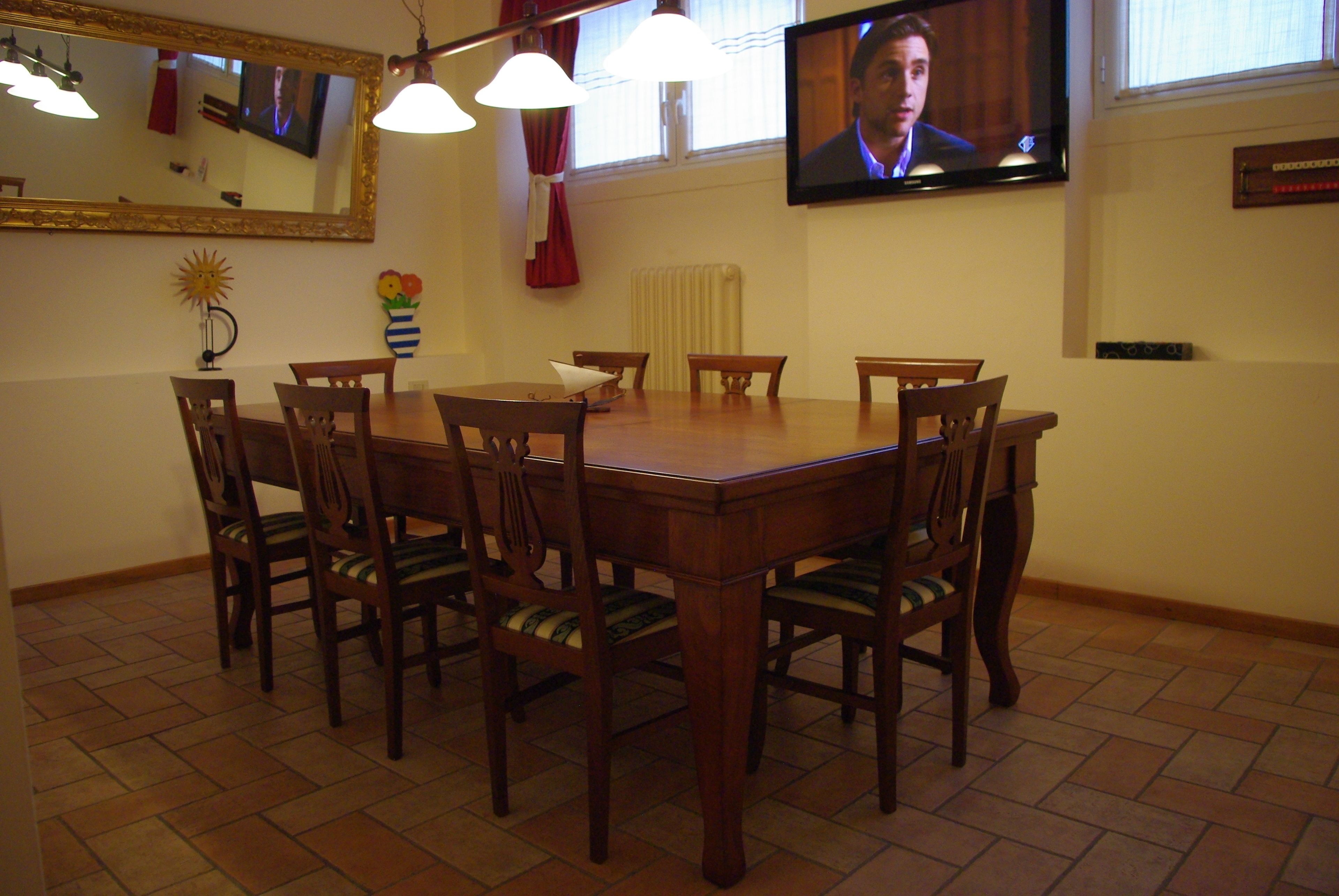 Un comedor con una mesa y sillas de madera, un televisor montado en la pared y un espejo sobre la mesa.