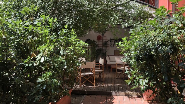 A patio area with a wooden table and chairs, surrounded by lush green plants. - Il Girasole (Milan)