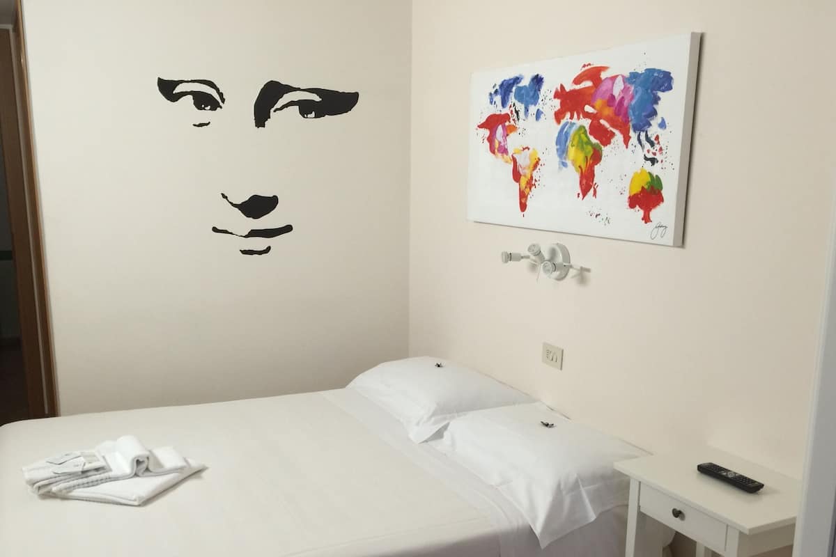A hotel room with a bed, a wall-mounted world map, and a wall decal of a face.