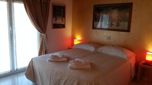 A hotel room with a large bed, two bedside lamps, a painting on the wall, and a window with curtains. - Il Girasole (Milan)