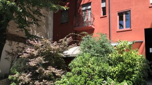 A red building with a balcony, surrounded by various potted plants and trees. - Il Girasole (Milan)