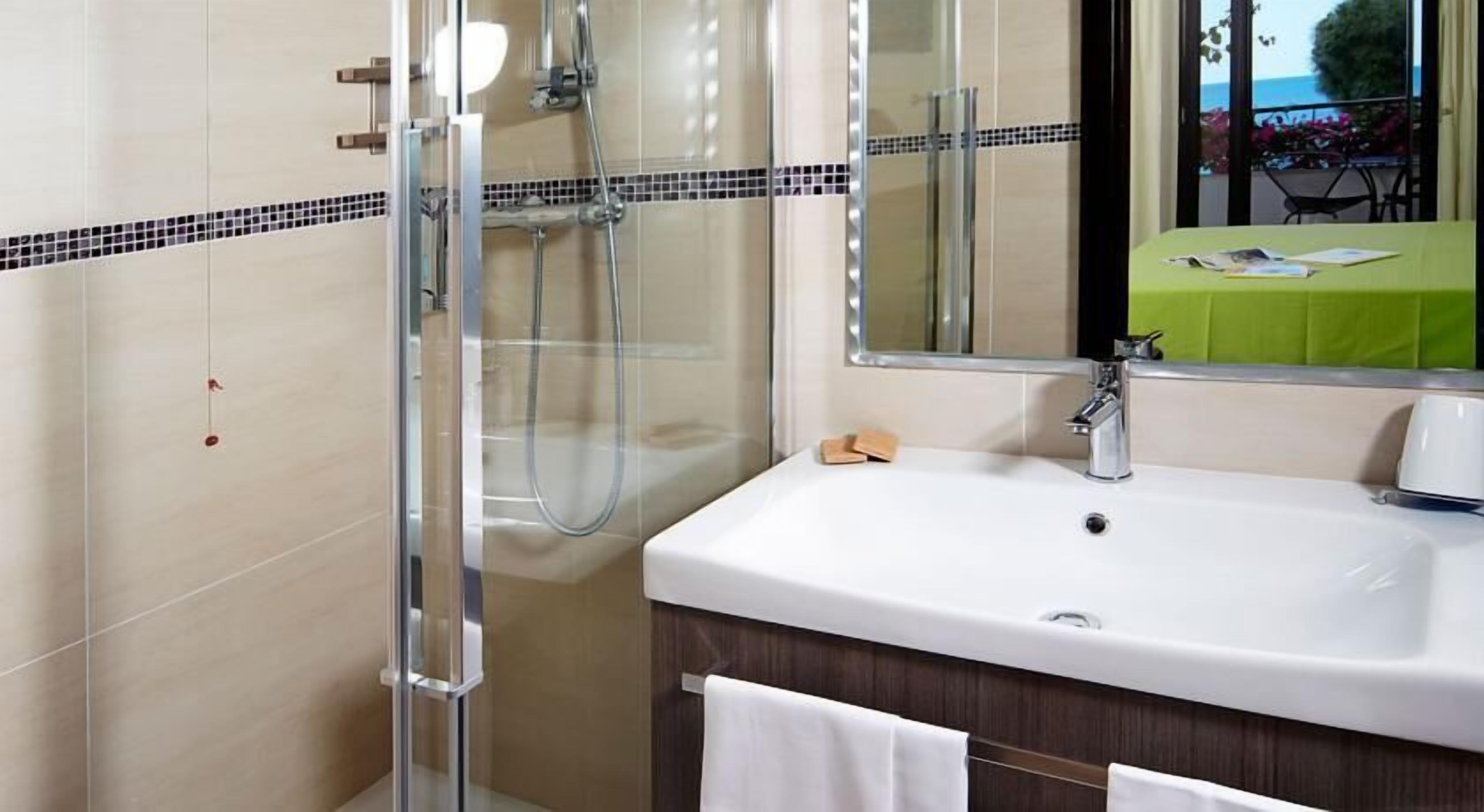 A bathroom with a glass-enclosed shower, a white sink, and a mirror reflecting a balcony with a table and chairs.