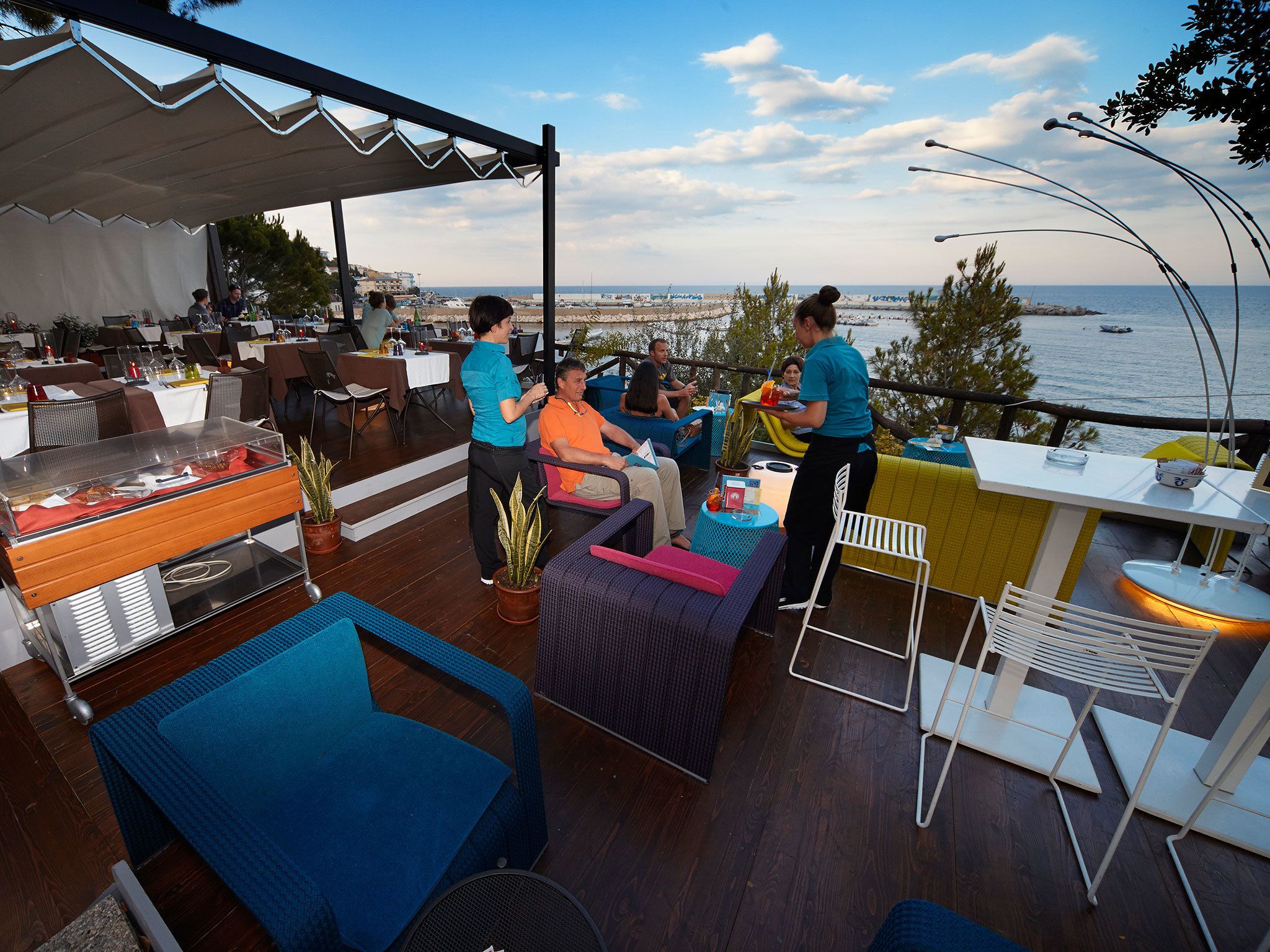 Uma área de refeições ao ar livre com vista para o mar, equipada com cadeiras e mesas, e um buffet.