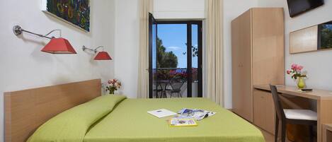 A hotel room with a bed, a desk, a chair, a TV, and a balcony with a view.