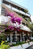 Un edificio moderno con balcones, un jardín lleno de flores y un cielo despejado.