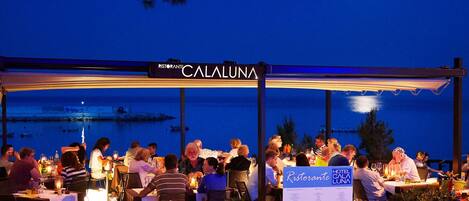 Ein Essbereich im Freien im Ristorante Calaluna mit gedeckten Tischen für Gäste mit Blick auf ein Gewässer.