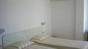 Een eenvoudige kamer met een bed, een wandairconditioner en een effen muur.