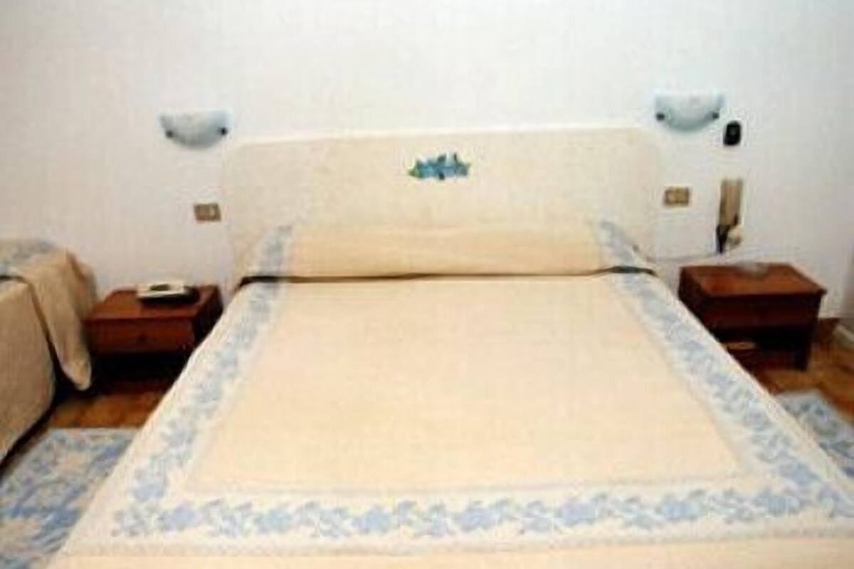 Una habitación de hotel estándar con una cama individual, dos mesitas de noche y una mesita auxiliar.