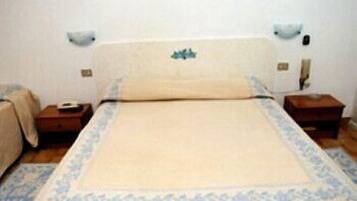 Una habitación de hotel estándar con una cama individual, dos mesitas de noche y una mesita auxiliar.