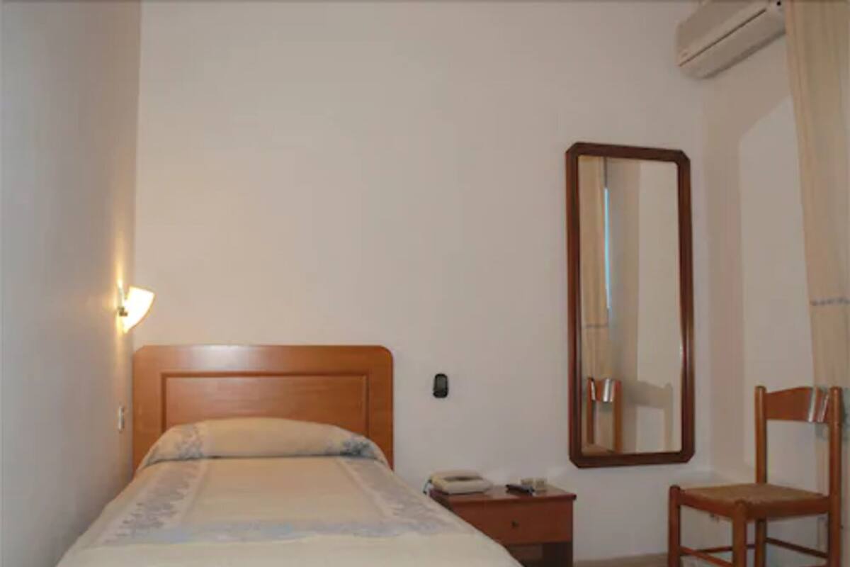 Un dormitorio con cama, mesita de noche, silla, espejo y aire acondicionado.