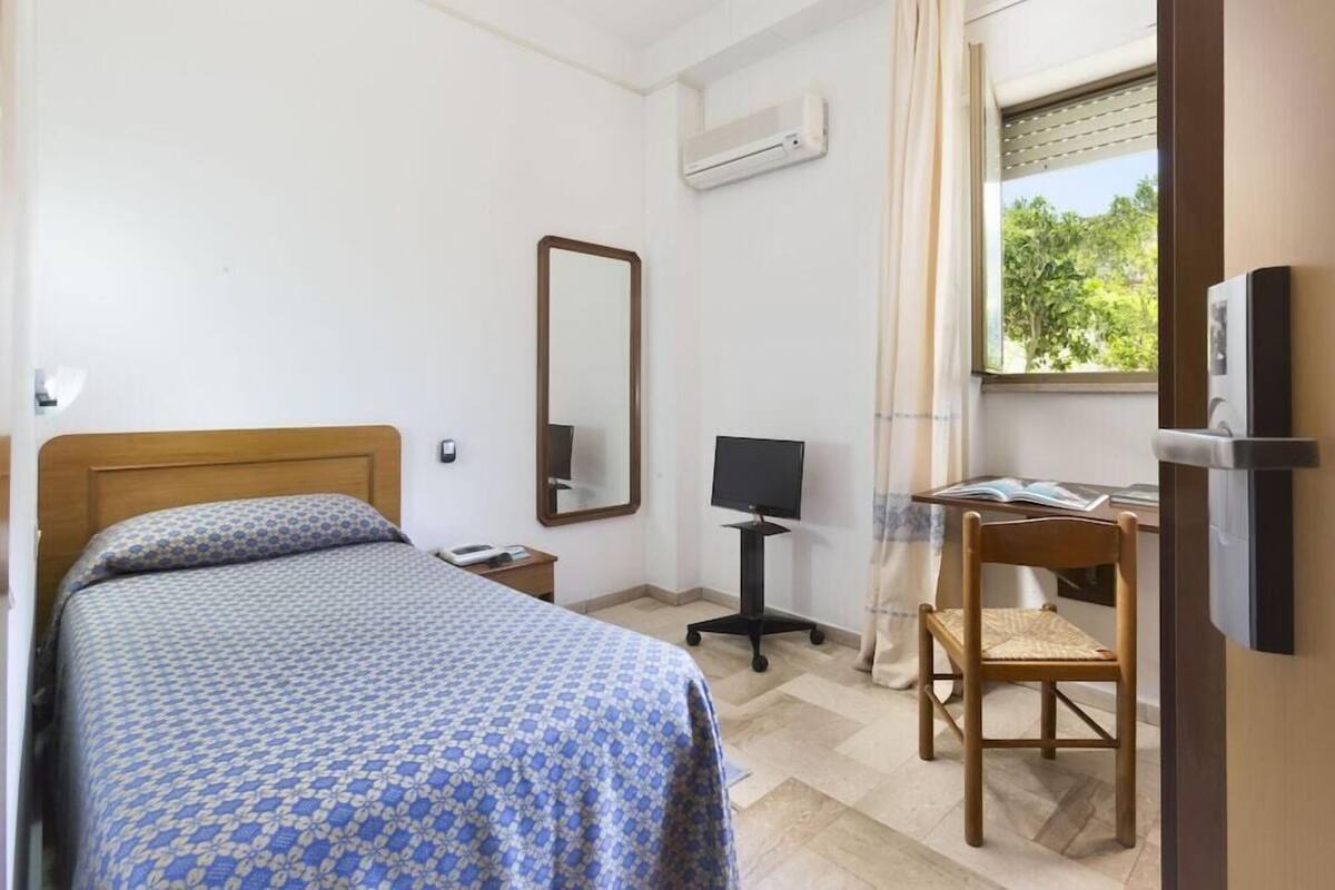 Un dormitorio con una cama, un escritorio con computadora, una silla, un espejo y un aire acondicionado.