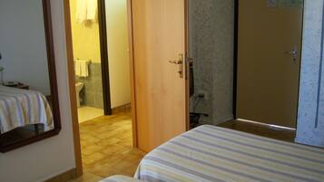 Een hotelkamer met twee bedden, een badkamer en een deur die naar een andere kamer leidt.