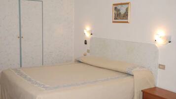 Une chambre à coucher avec un lit, une table de chevet, une lampe fixée au mur et une porte.