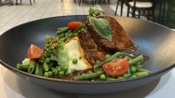 Comedor con mesas y sillas, un ventanal grande y un plato con carne y verduras.