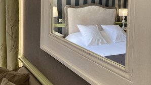 Una habitación de hotel con un espejo grande que refleja una cama con ropa blanca y una pared a rayas al fondo.
