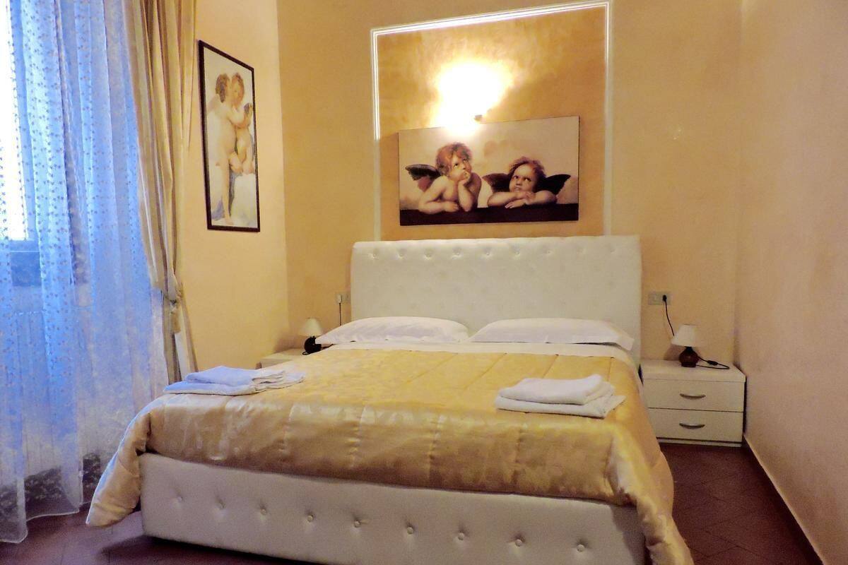 A bedroom with a large bed, a bedside table, a nightstand, and a wall-mounted light fixture.