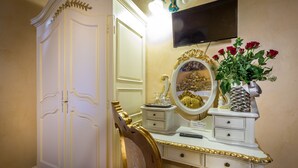Une pièce avec une coiffeuse blanche, un miroir à cadre doré, un vase de roses rouges et un téléviseur fixé au mur.
