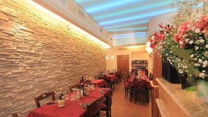 Un restaurant aux murs de pierre et aux nappes rouges, avec un long comptoir et des décorations florales.