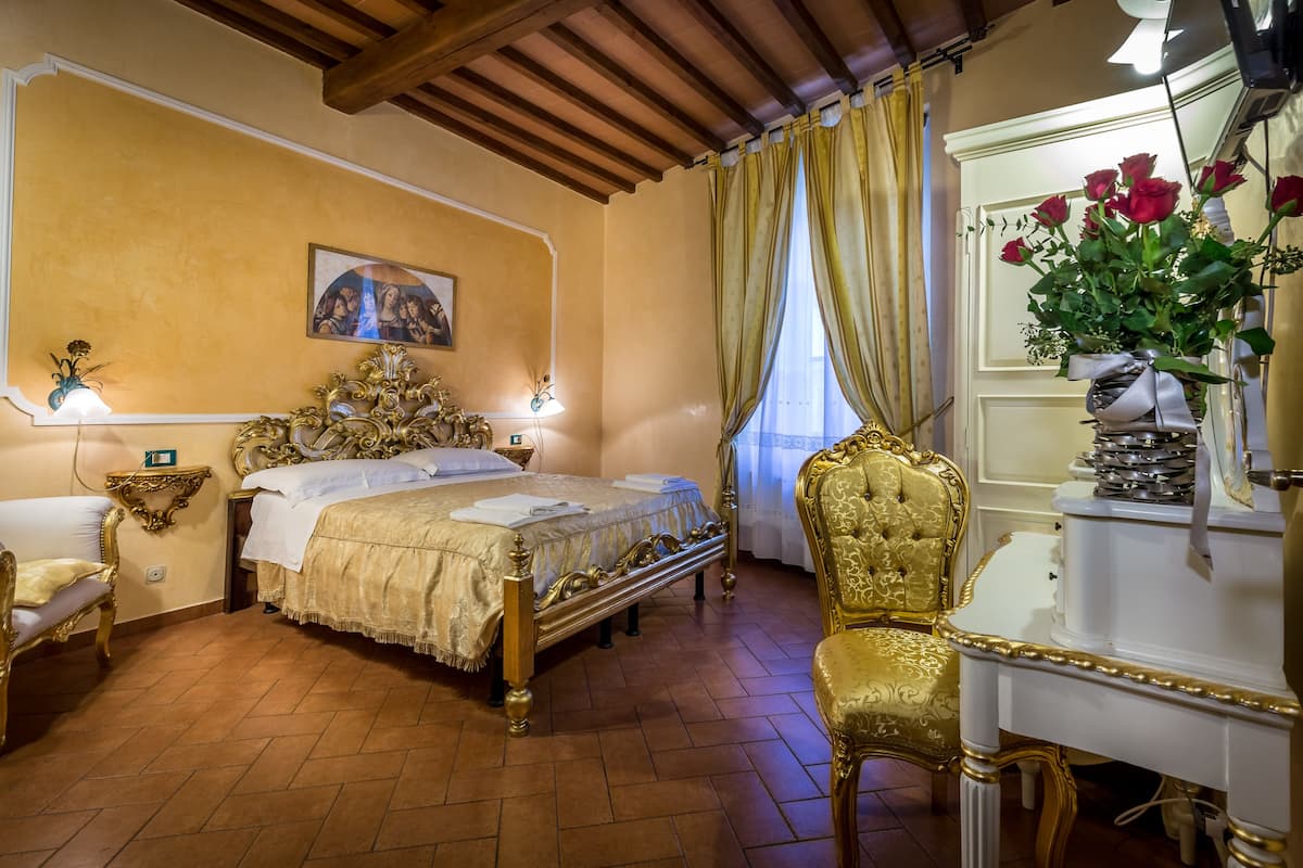 A room with a bed, a desk, a chair, a lamp, and a vase of flowers.