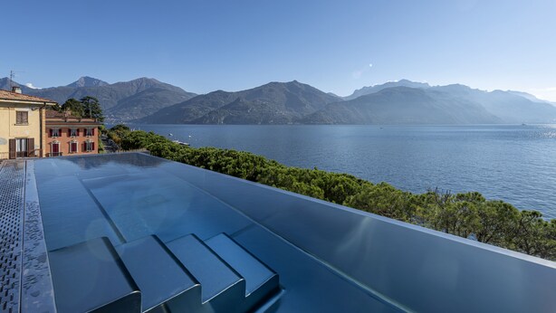 Piscina infinita no terraço com vista desobstruída para um lago e montanhas.