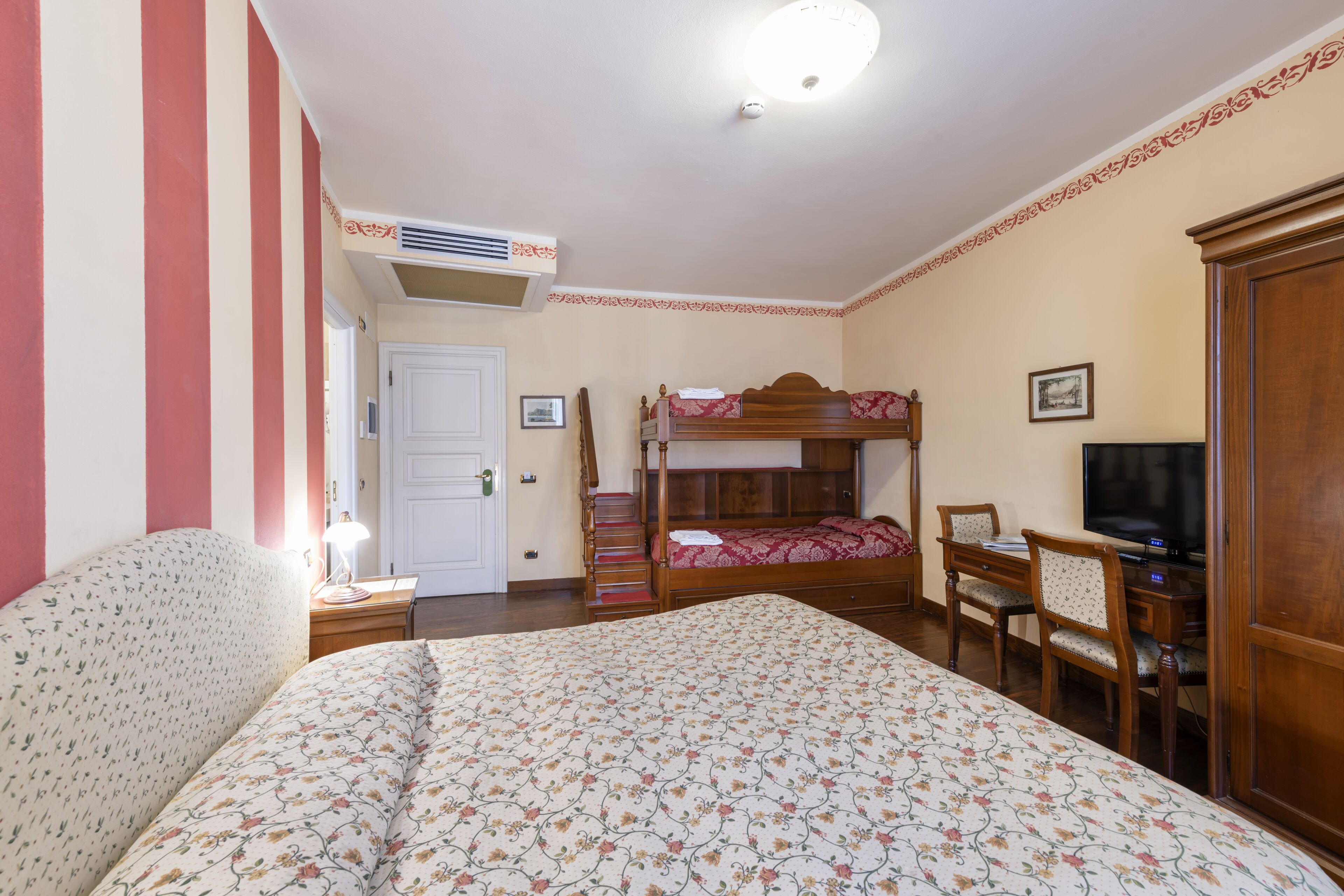 Un dormitorio con una cama litera, un escritorio con silla, un televisor y una mesita de noche con lámpara.