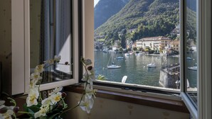 Vista pela janela de um lago com barcos, uma montanha e edifícios ao fundo.