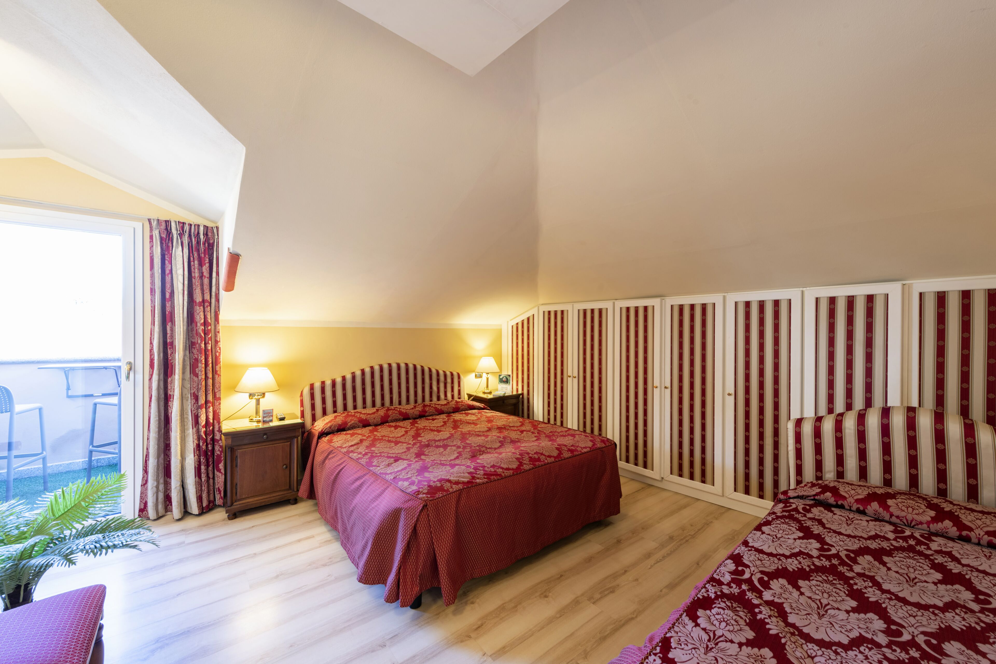 Habitación de hotel con una cama grande, una mesita de noche con lámpara, una pequeña mesa con una silla y vistas al exterior a través de una puerta corrediza.