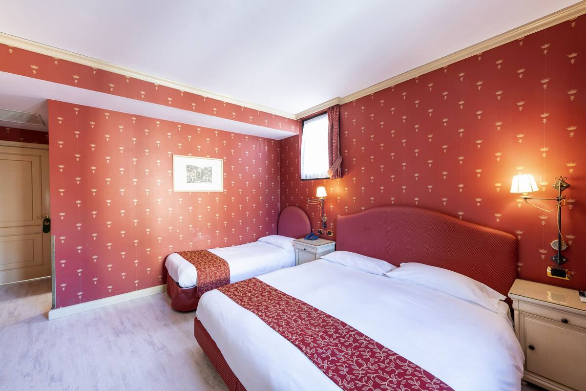 Una habitación de hotel con dos camas, una mesita de noche, una lámpara y un cuadro en la pared.