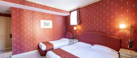 Hotellihuone, jossa on kaksi sänkyä, yöpöytä, lamppu ja seinällä oleva kehystetty kuva.