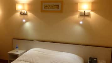 Ein Hotelzimmer mit einem großen Bett, zwei Nachttischen, einer Wasserflasche auf einem Tisch und einem Telefon auf dem anderen.