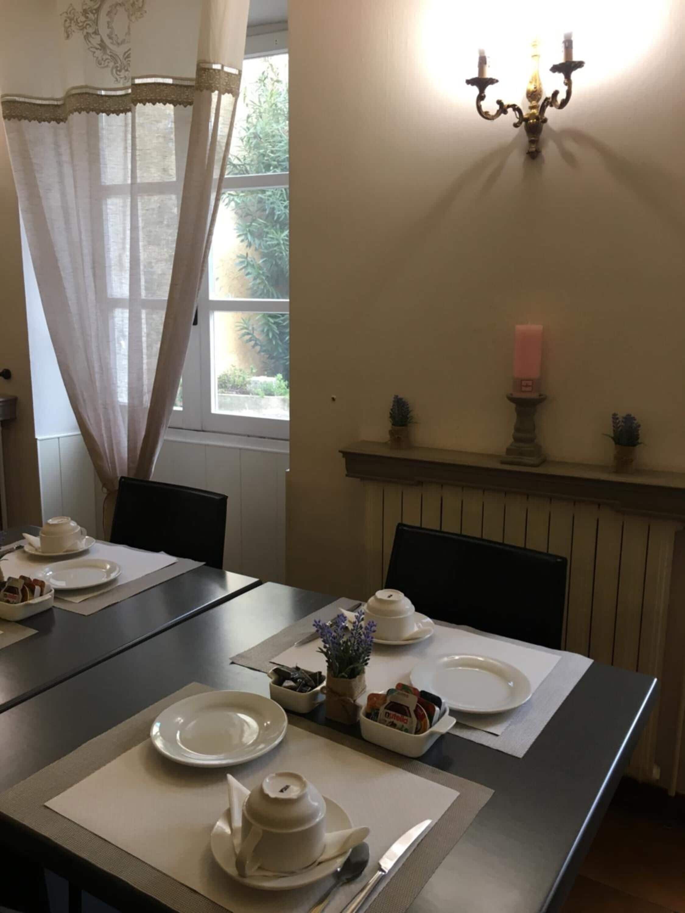 Un coin repas avec une table dressée pour deux personnes, comprenant des assiettes blanches, une théière et un petit vase avec des fleurs.