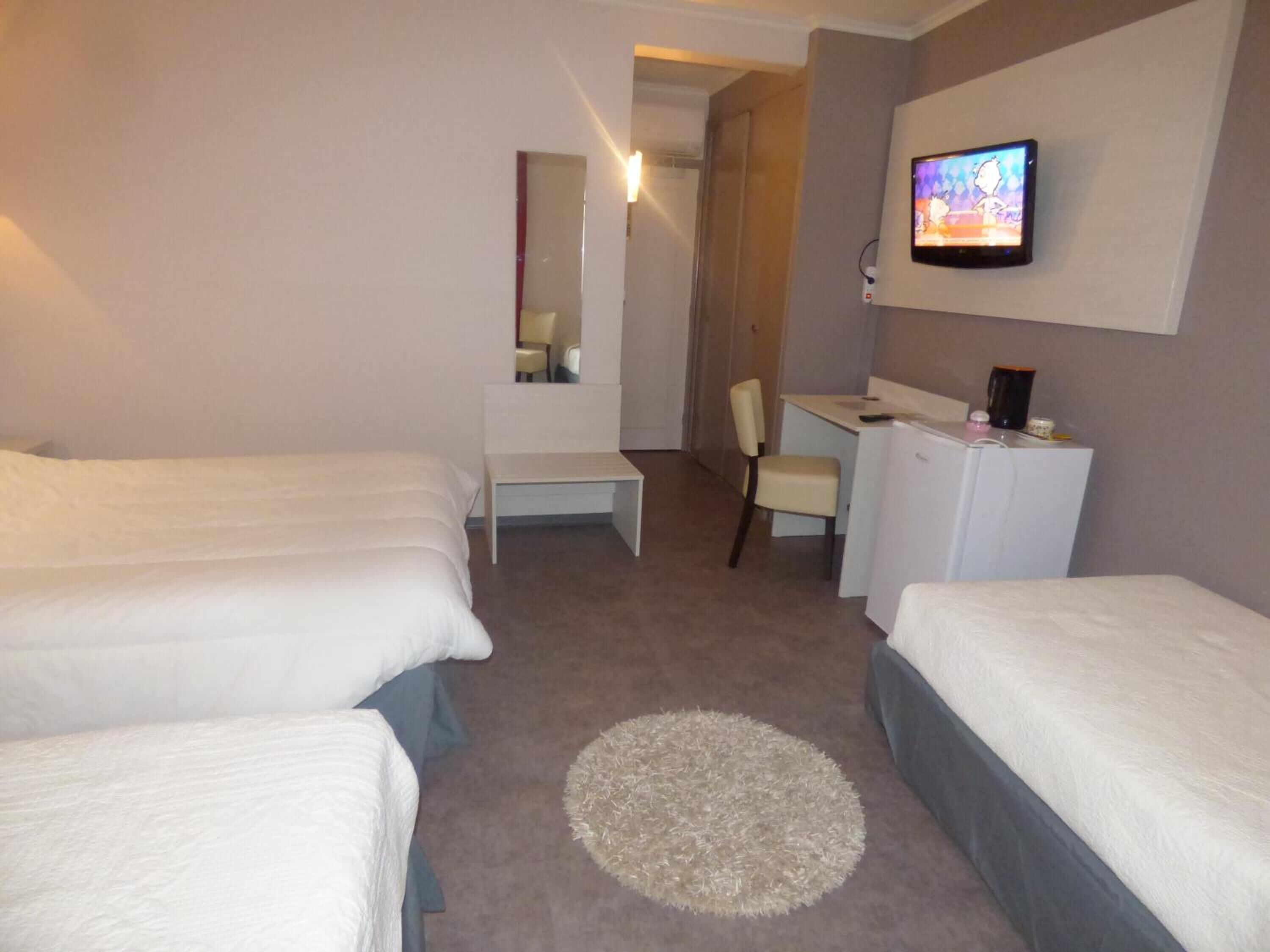 A hotel room with two single beds, a desk, a chair, a television, and a small refrigerator.