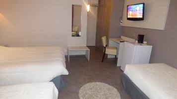 A hotel room with two single beds, a desk, a chair, a television, and a small refrigerator.