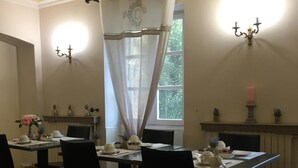 A dining area with tables set for a meal, a window with curtains, and wall-mounted sconces.