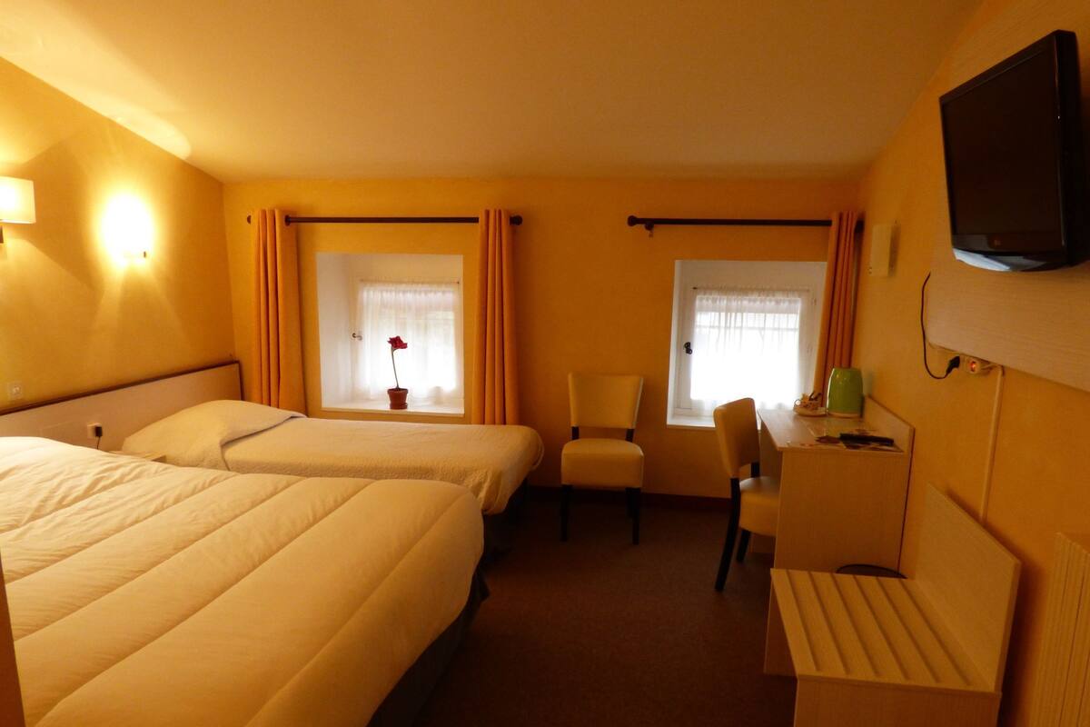 A hotel room with two beds, a desk, a chair, and a television.