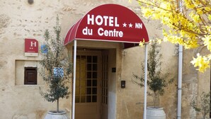 A hotel entrance with a red awning, a door, and two potted plants.
